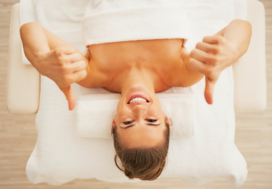 Portrait of happy young woman laying on massage table and showing thumbs up