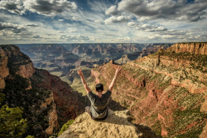 Grand Canyon and a happy hiker on the rim with arms raised up. Winner, success and achievement concept in nature.