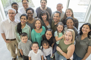 A multi-ethnic group of multi-generational families are standing together in a group and are smiling while looking at the camera.