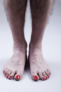 Man's Feet with Red Nail Polish and Hairy Legs on Bright Gray Background