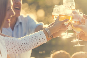 Group of friends having drinks at sunset. They are celebrating with a wine toast. They are smiling and happy. Lens flare