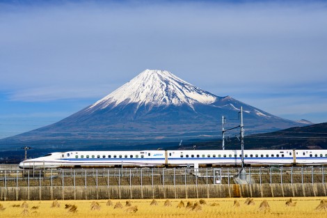 Fuji, Japan - December 14, 2012: A Shinkansen bullet train passes below Mt. Fuji through farmland. The Shinkansen is considered the world's busiest high speed rail line.