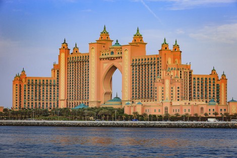 Dubai, United Arab Emirates - April 04, 2012: Atlantis, The Palm, the luxury five star hotel located on the outer crescent of the man made island, the Palm Jumeirah in the Arabian Gulf city of Dubai, in the United Arab Emirates. In the foreground the waters of the Persian Gulf and date palms transplanted to create a man made garden in front of the hotel. Some traffic and people can also be seen. Photo shot from a boat at an off-shore location, in the afternoon sunlight. Horizontal format; copy space.