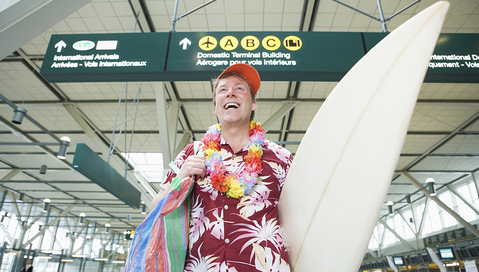 Man carrying surfboard in airport, smiling