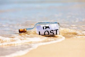 A bottle containing a confused message saying "I'm lost" is stranded in the surf at water's edge on a beach. .