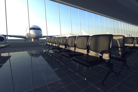 Modern airport terminal with black leather seats on a sunny morning. A huge viewing glass facade with a passenger aircraft behind it.